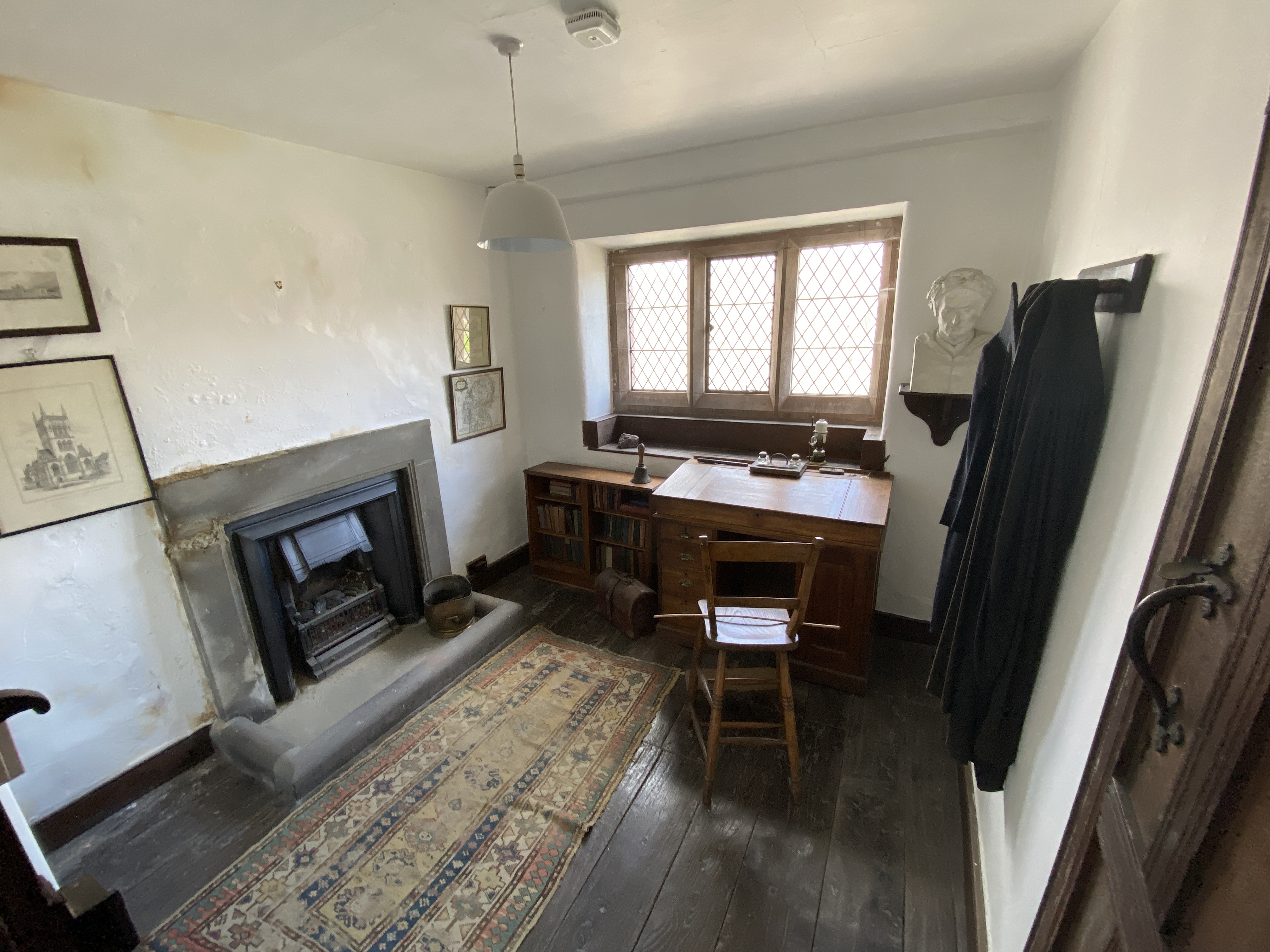 Photograph of the Headmaster's Study. A small room with white walls, a window, a wooden desk and bookcase. 